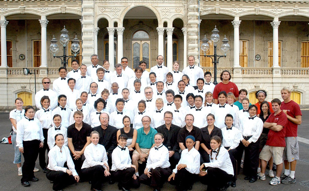 A group of people in white shirts and bow ties smiling together for a photo.