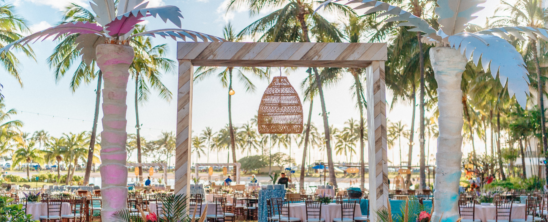 A beautiful reception under palm trees, featuring elegant chairs arranged for guests to enjoy the celebration.